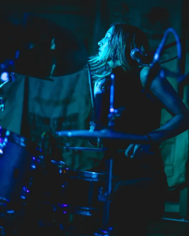 Michelle Milo playing drums on stage under blue light