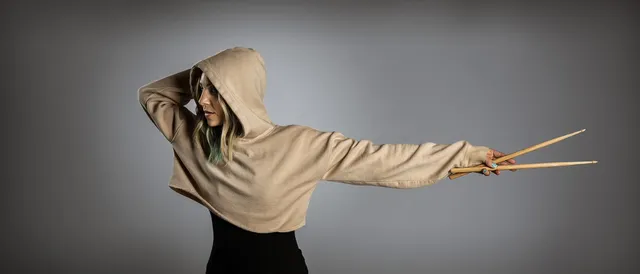 Michelle Milo extending a pair of drumsticks toward the camera