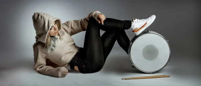 Michelle Milo in a sand-colored hoodie reclining beside a snare drum