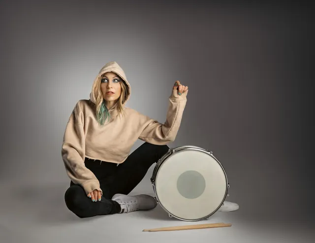 Michelle Milo seated beside a snare drum, hood up, looking upward